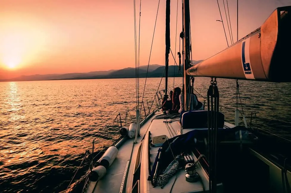 figures watch sunset from bow of sailboat