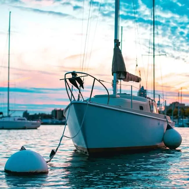 white sailboat at mooring buoy with pink sky