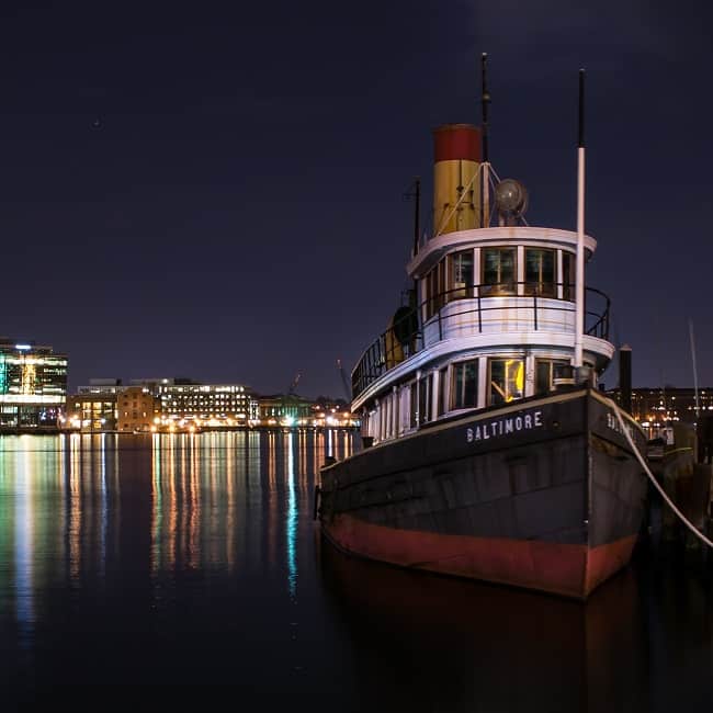 tug boat with black and red hull and city lights in the background