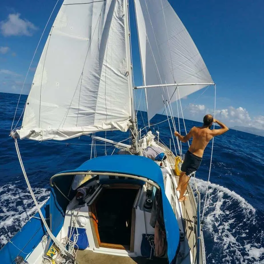 Man standing on side of sailboat looking out to sea