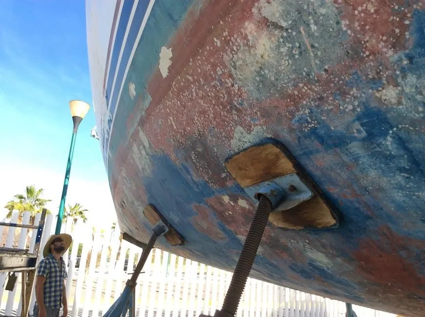 man in a hat looking at the hull of a boat in a boat yard
