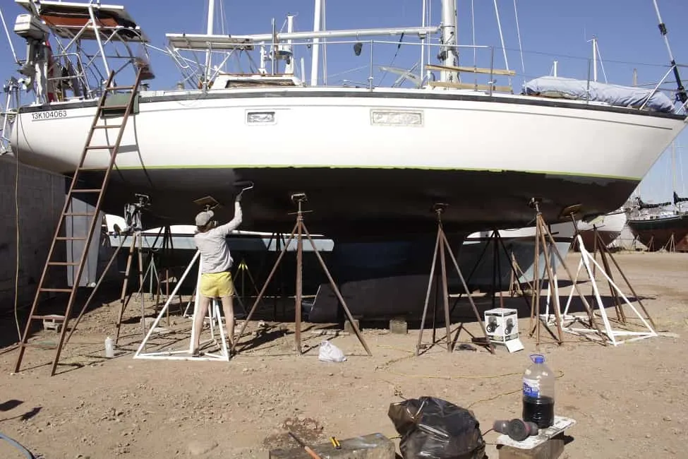 Woman painting a sailboat hull with black paint