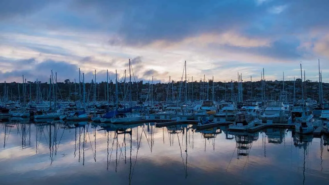 boats in a marina with cloudy sky and rock pier in background