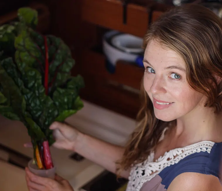 woman putting kale in glass of water in sailboat galley