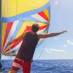Man in red shorts standing behind a yellow, blue, red, and white spinnaker