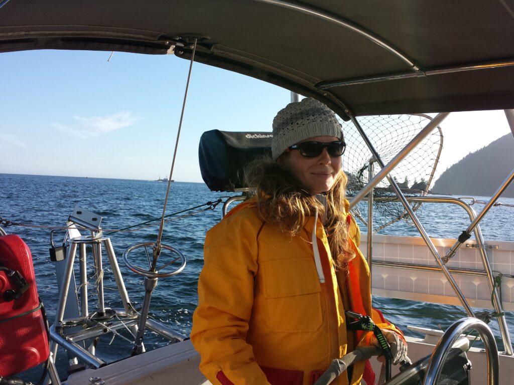 Woman in yellow float suit at the helm of a sailboat