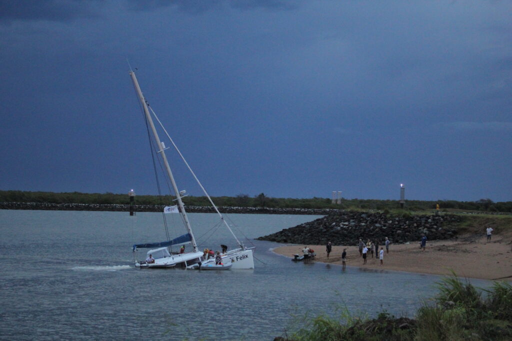 People on beach and sinking catamaran sailboat
