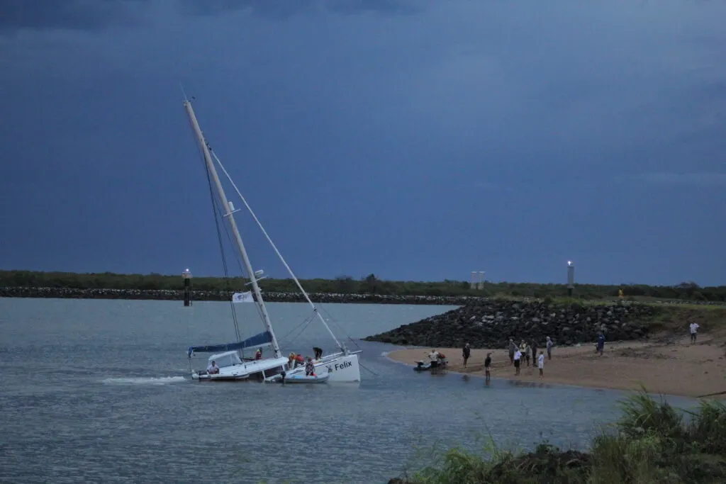People on beach and sinking catamaran sailboat