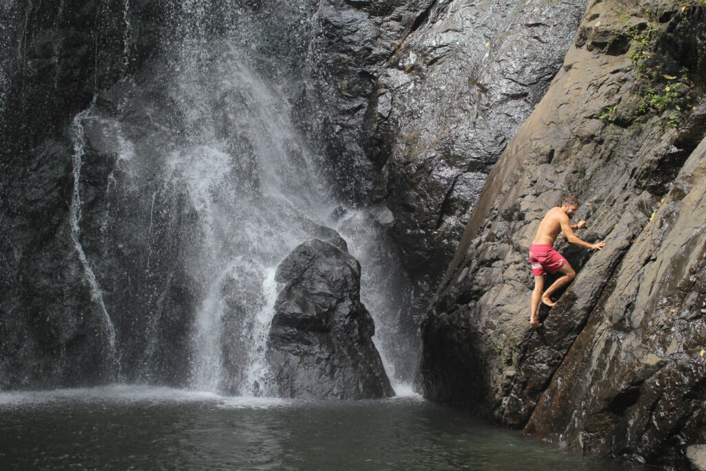 Man in red shorts climbing rock next to waterfall
