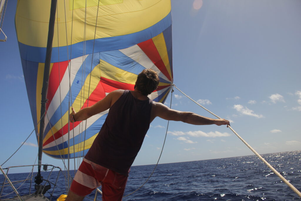 man standing in front of red, yellow, and blue asymmetrical spinnaker on a sailboat