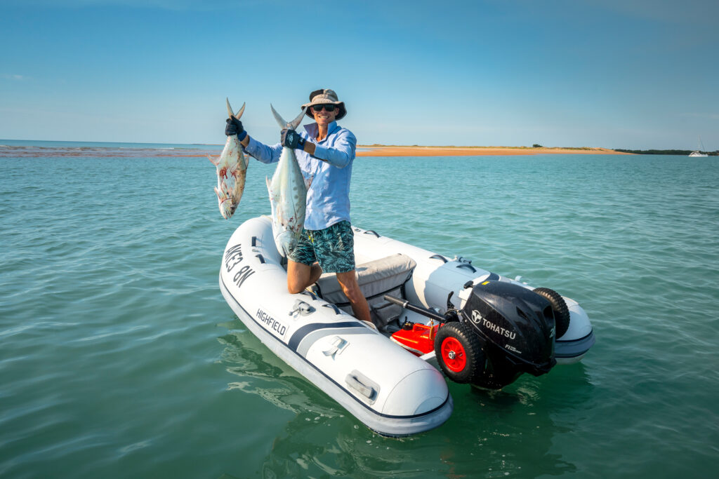 man holding two fish in inflatable dinghy