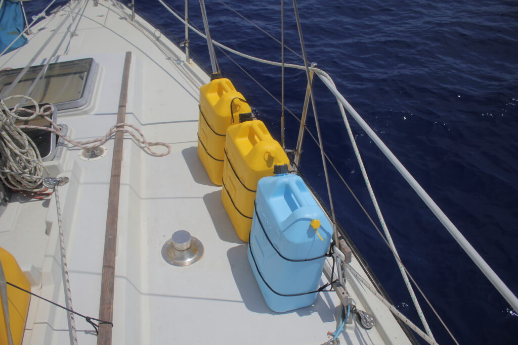 two yellow diesel jugs and one blue water jug tied down on the deck of a sailboat