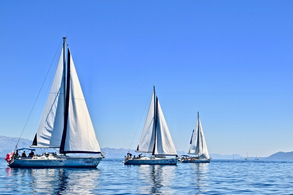 three sailboats with a blue sky and water