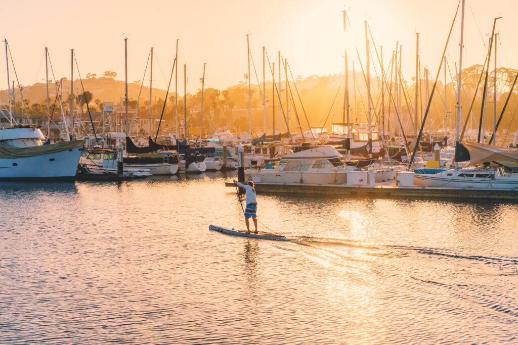 Paddle boarder paddling by a marina in golden light